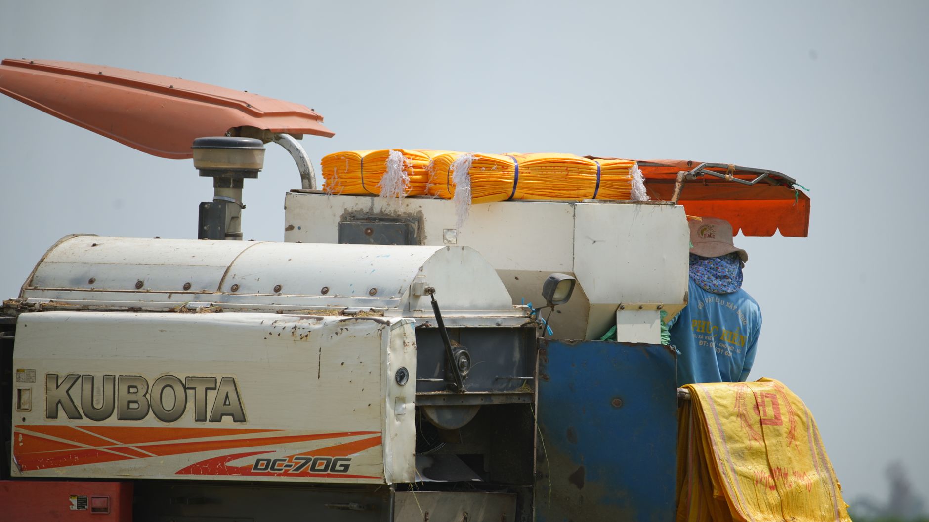 Side view of a Kubota harvester with a farmer in a field, showcasing agricultural machinery.