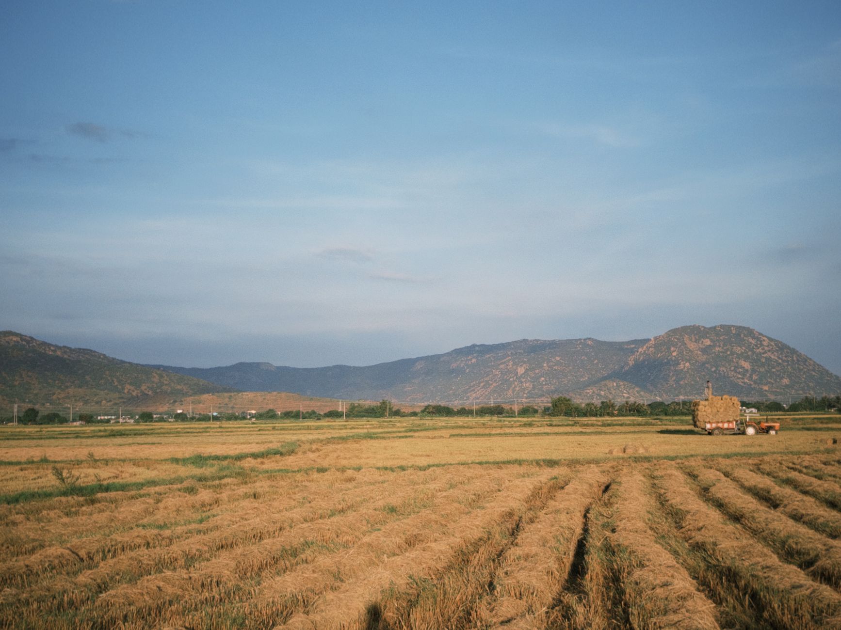 Expansive rural farmland with hay bales under a clear sky, set against a mountain backdrop.