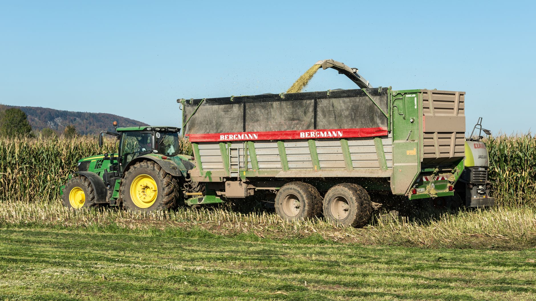 A tractor harvesting corn in a rural field in Paderborn, Germany on a sunny day.
