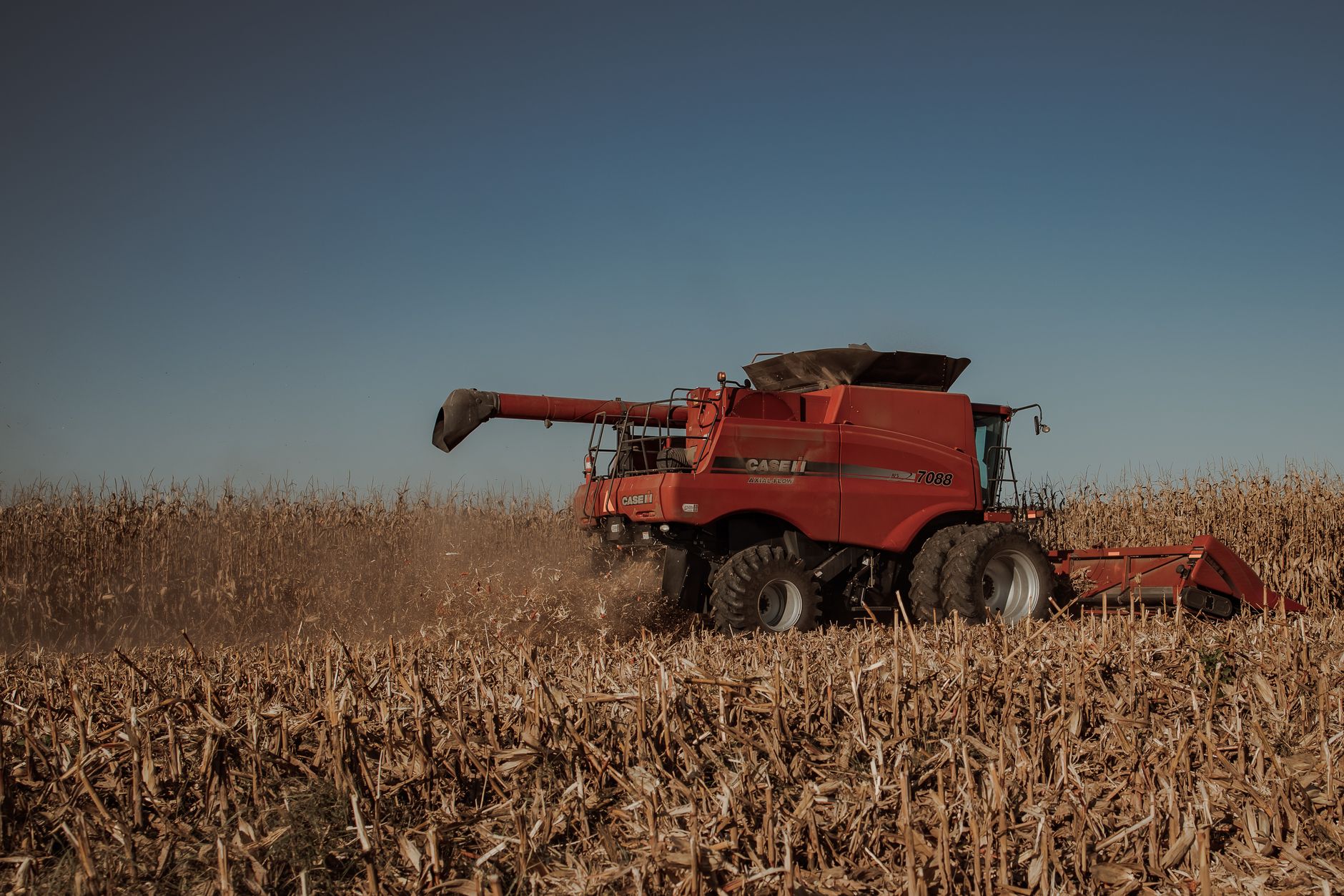 Red combine harvester harvesting corn under a clear sky, showcasing modern agriculture.