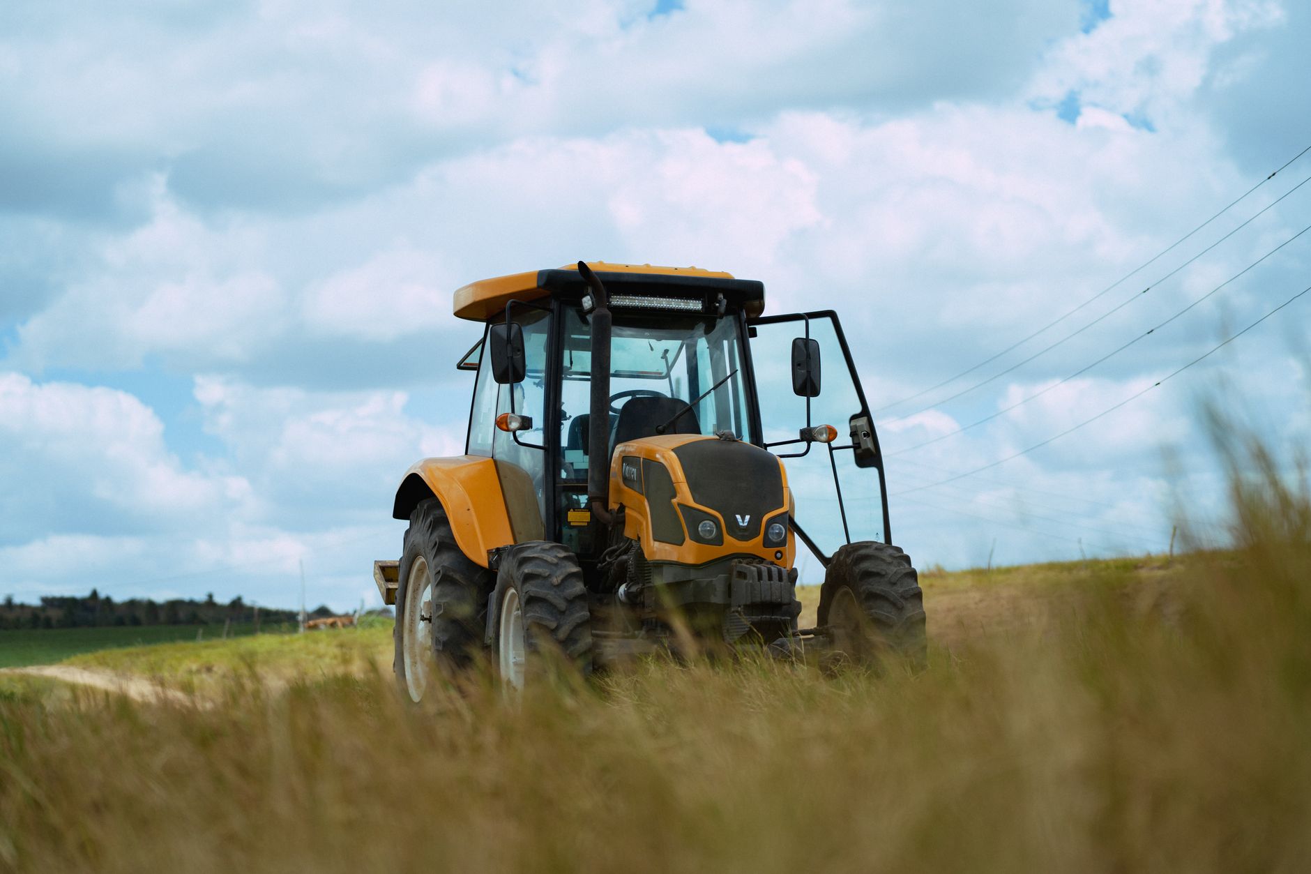 A vibrant yellow tractor in an open field showcases modern agricultural machinery under a cloud-speckled blue sky.