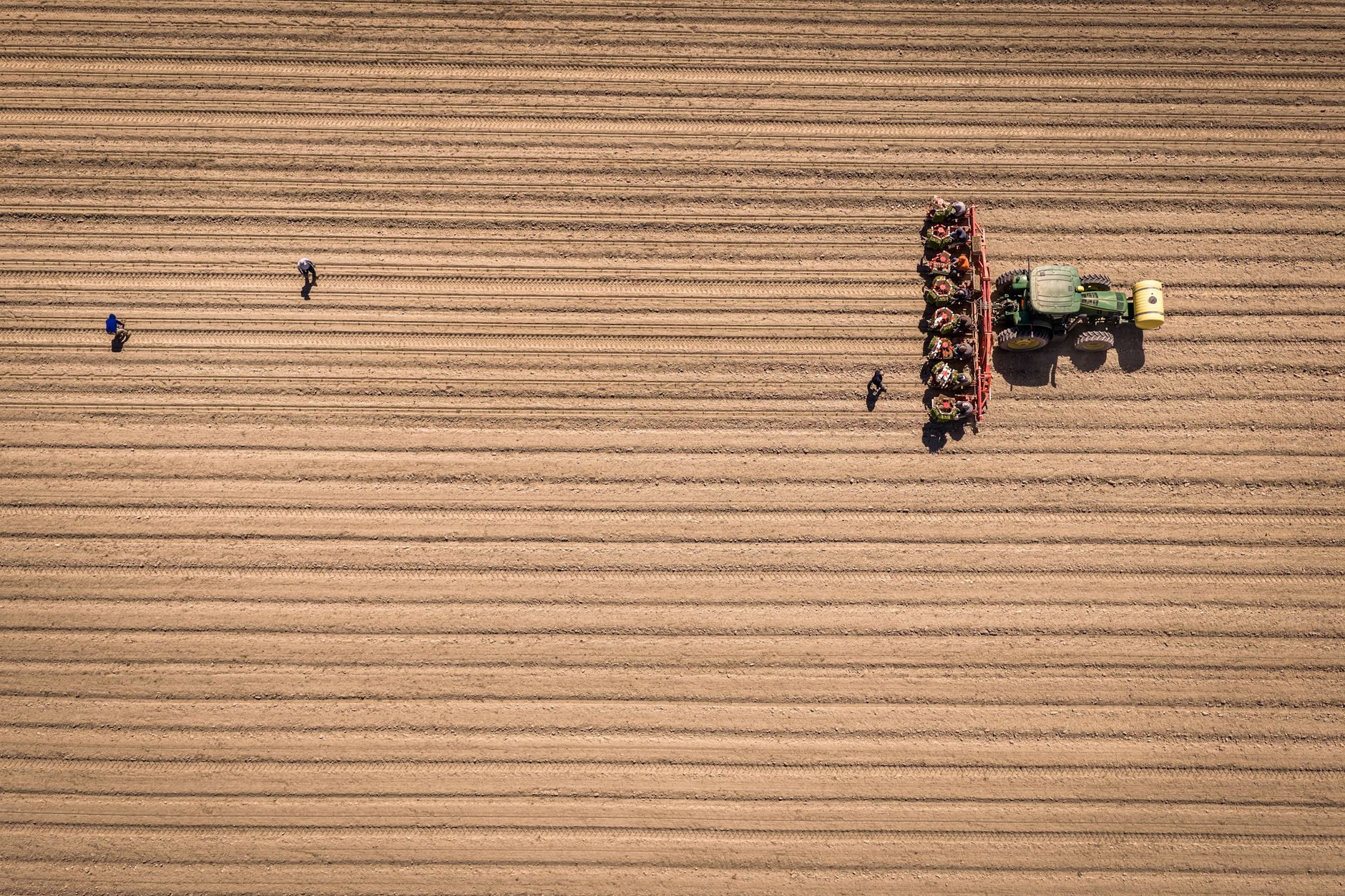 An aerial shot of a plowed field featuring a tractor and workers, showcasing agricultural machinery and farming activity.
