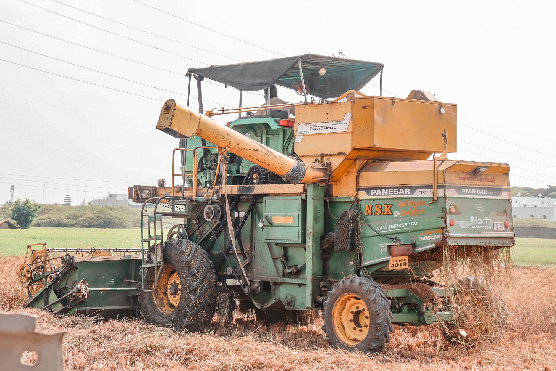 A side view of a combine harvester working in a rural field during the grain harvest season.