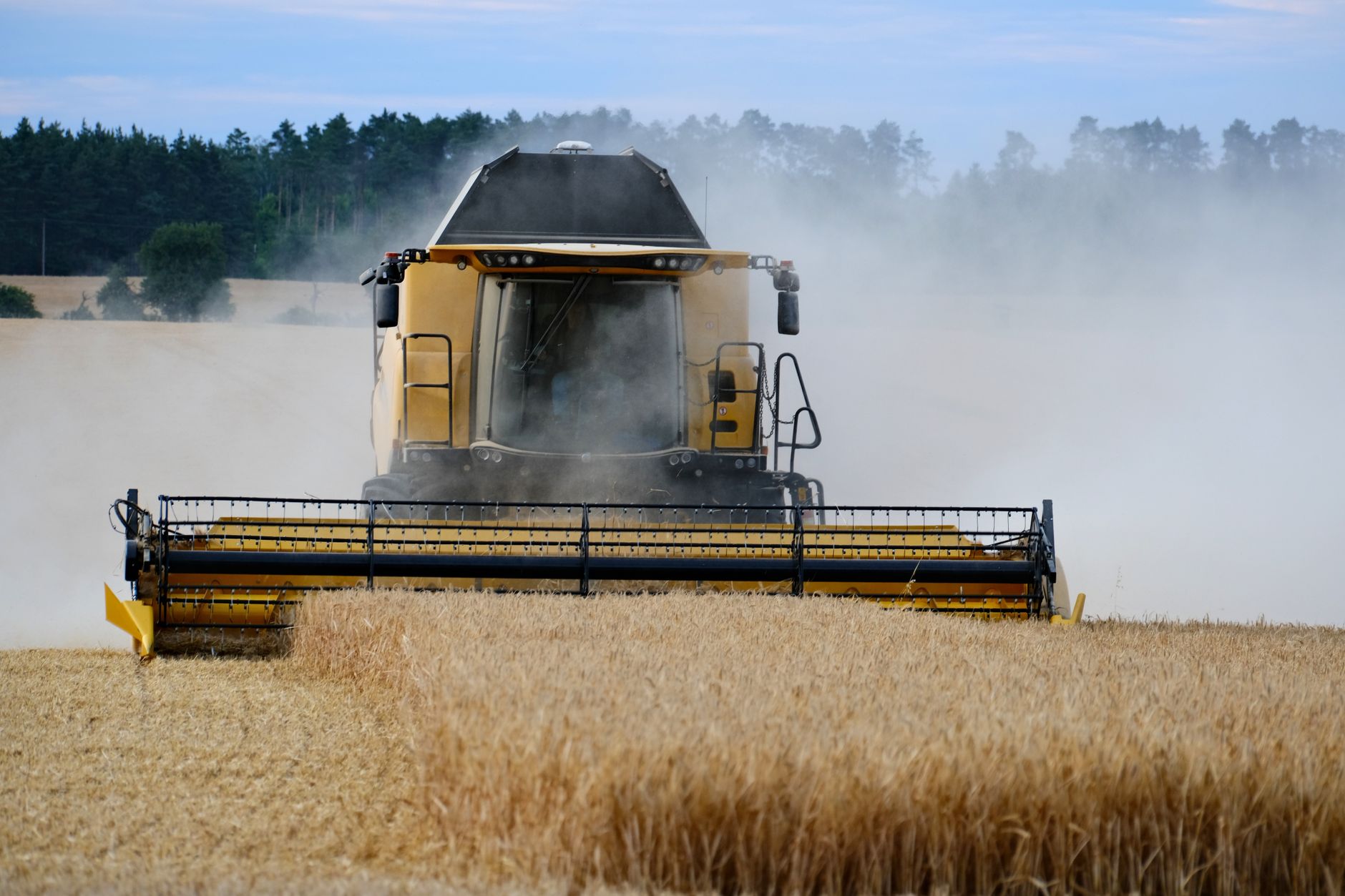 A combine harvester cutting through a dusty wheat field outdoors during daytime.