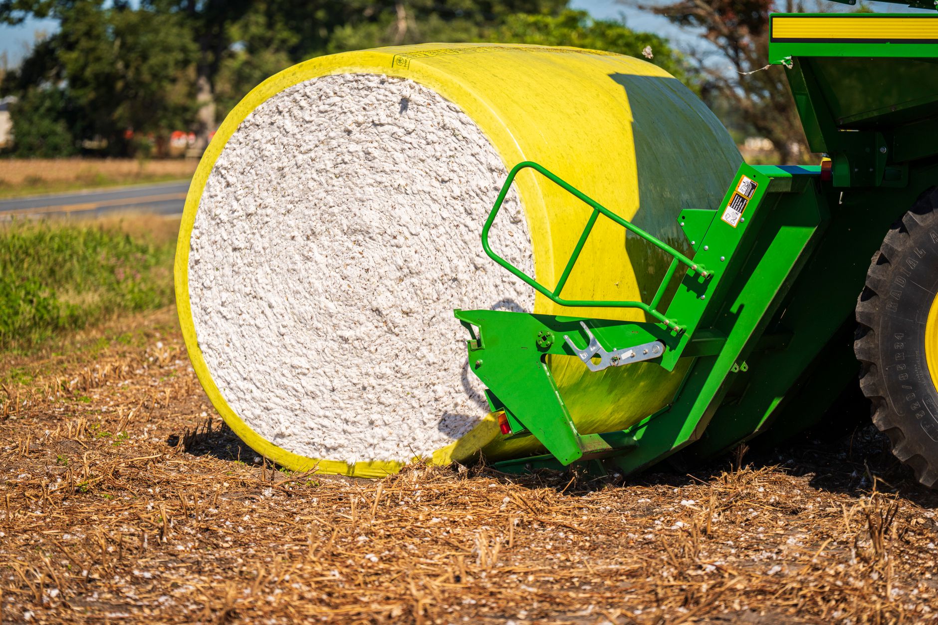 Close-up of a cotton bale next to green agricultural machinery in an open field.