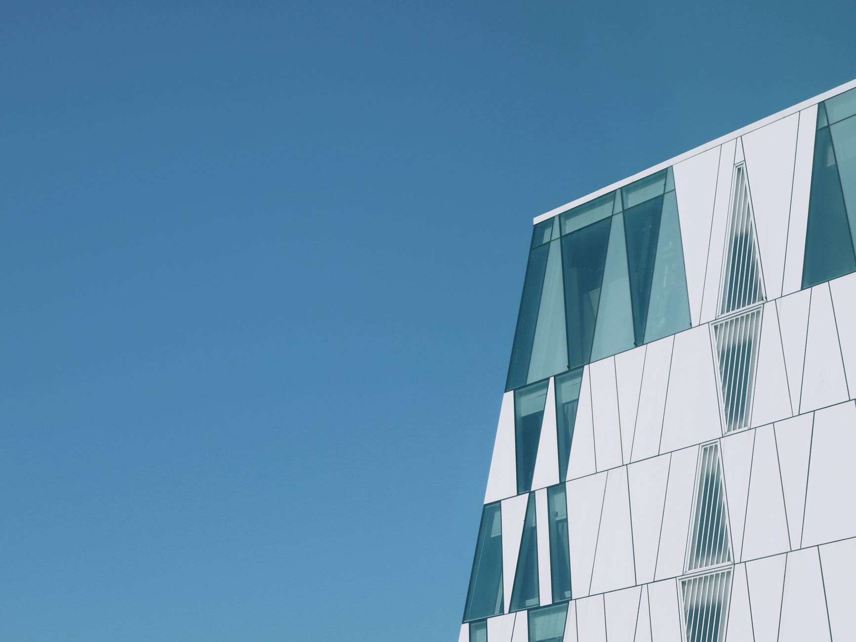 Geometric modern building with reflective glass in Copenhagen, Denmark, under bright blue sky.