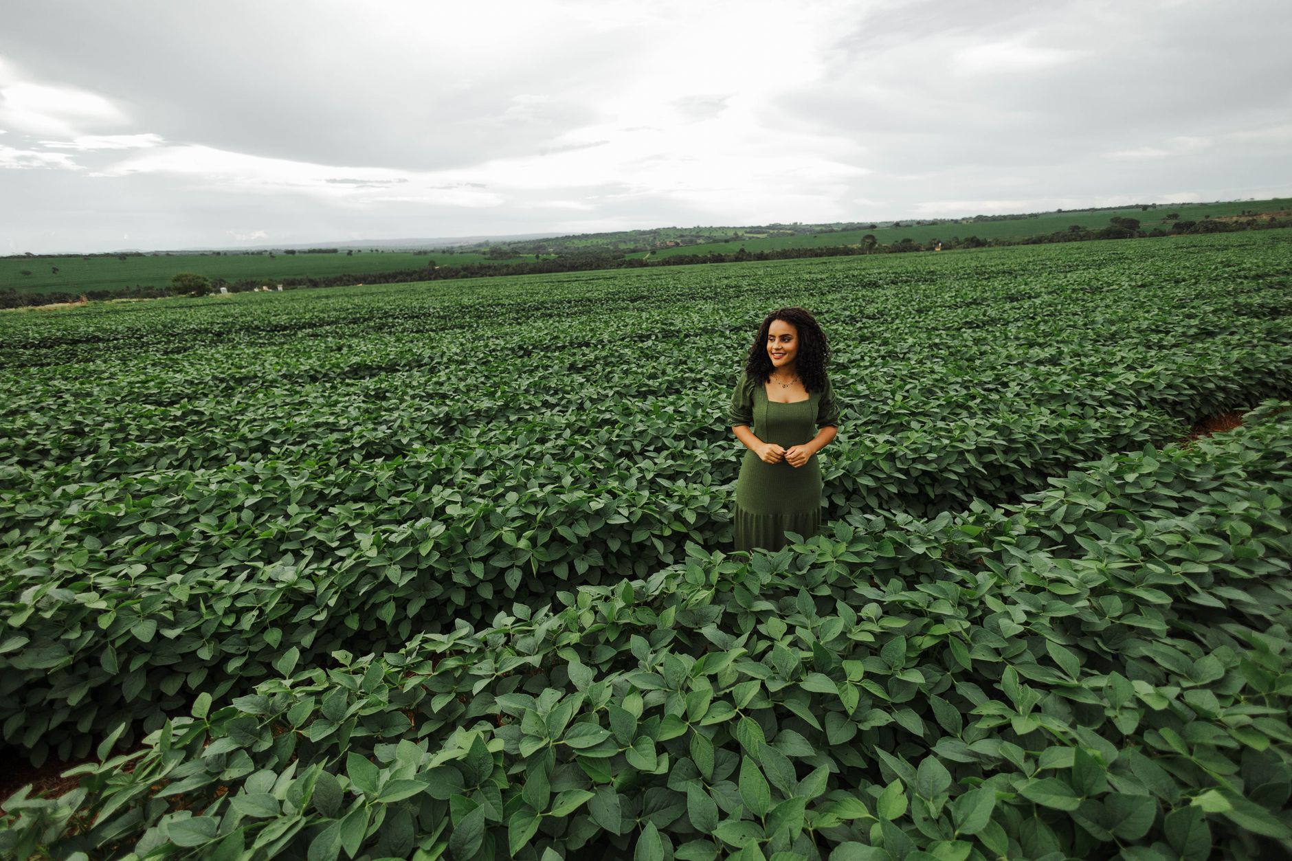 A woman smiling in a lush green cropland field, symbolizing relaxation and rural life.