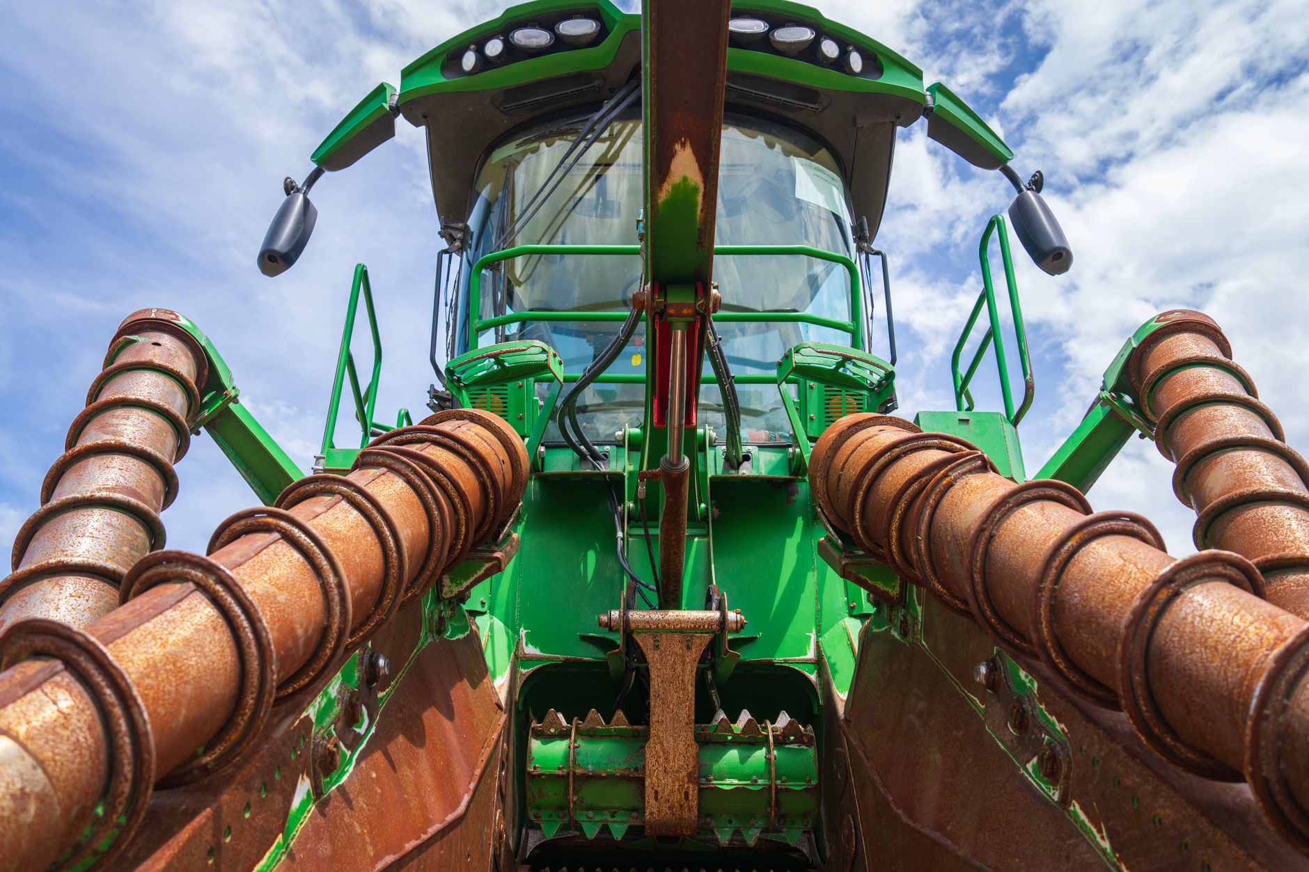 Detailed view of a green agricultural harvester against a blue sky, highlighting its machinery components.