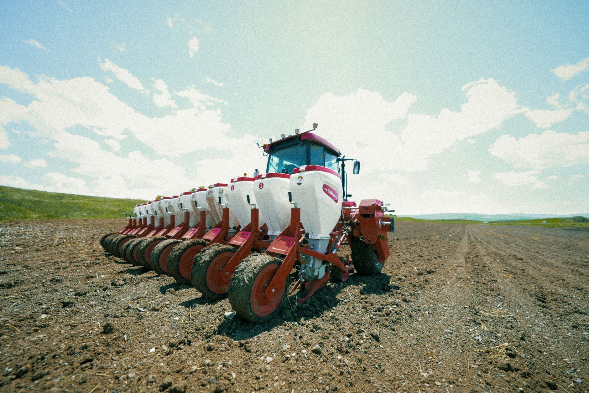 A modern tractor prepares soil in the expansive farmlands of Erzurum, Türkiye under a clear blue sky.