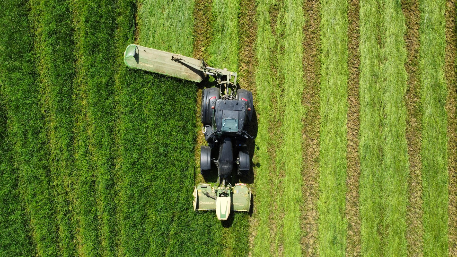 Aerial shot of a tractor mowing a lush green field, capturing the beauty of agriculture.