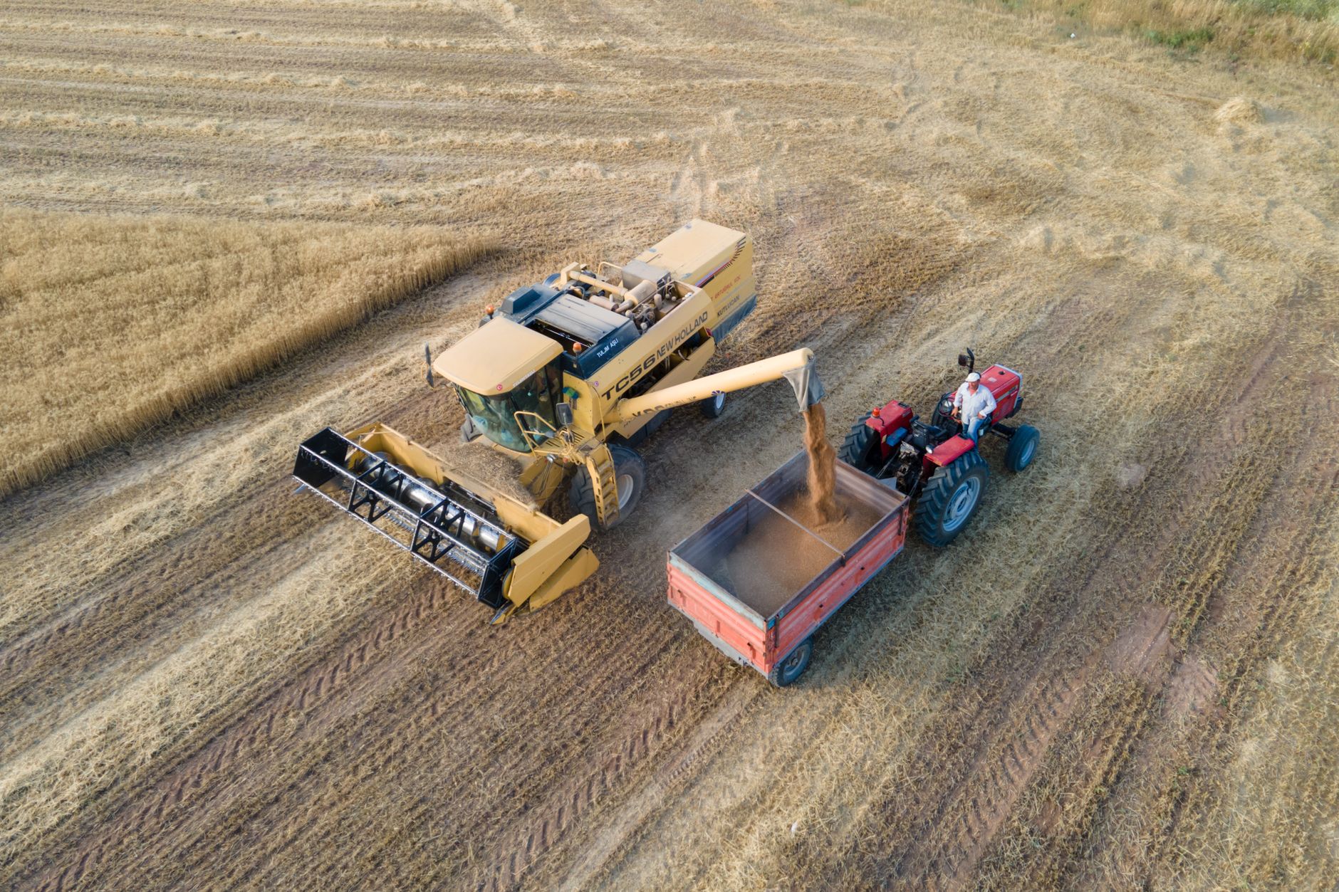 Aerial shot of a combine harvester and tractor working together in a field during harvest.