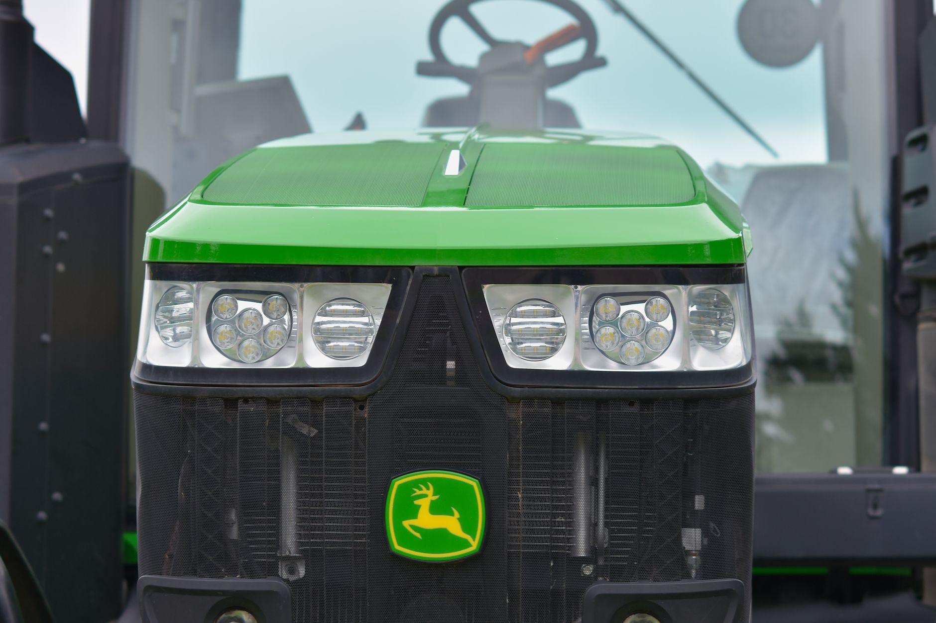 Detailed close-up of a green tractor's front grill featuring headlights, captured outdoors in daylight.