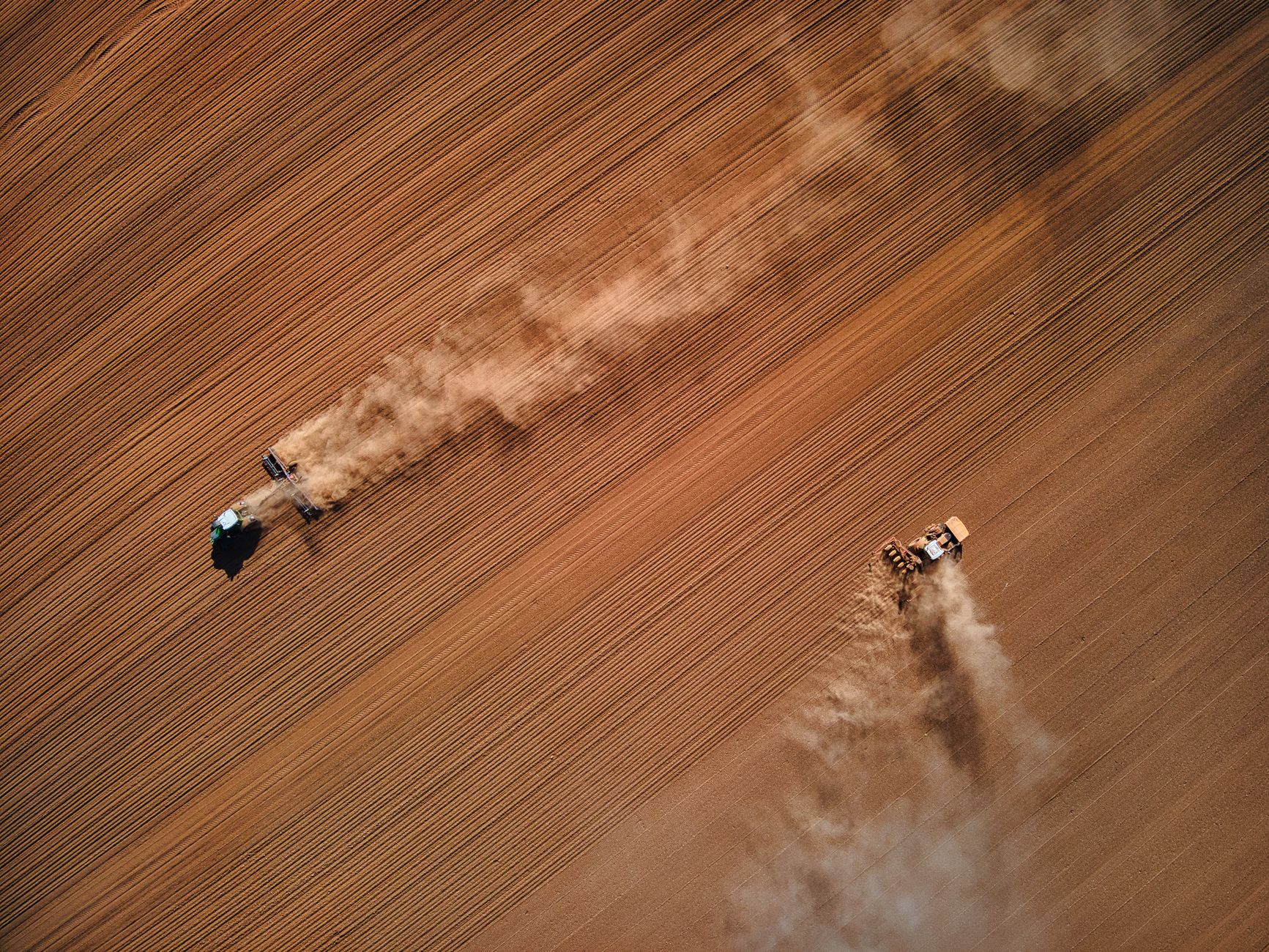 Aerial shot of two tractors working on a dusty field in the Peak District, UK.