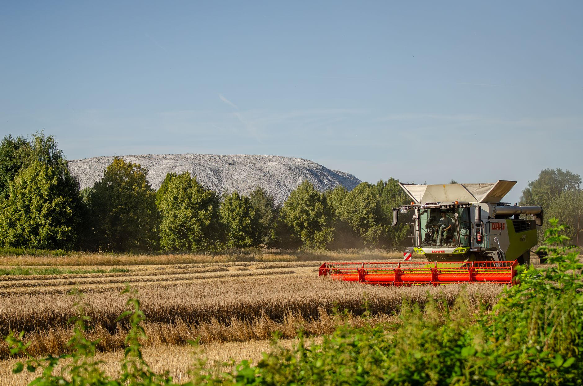 Combine harvester working in a lush rural field during summer with a scenic backdrop.
