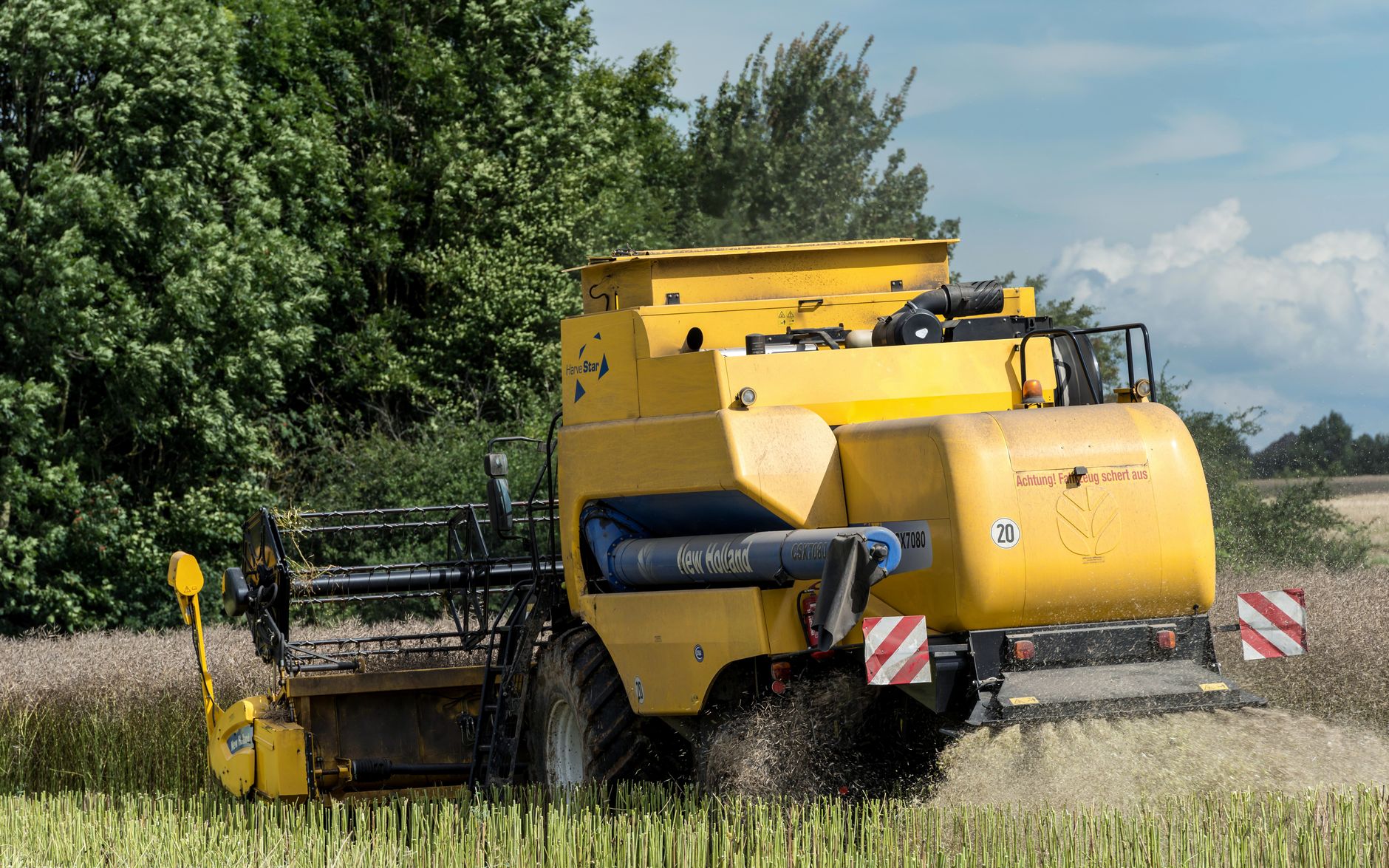 A yellow combine harvester working in a lush, green field in Germany.
