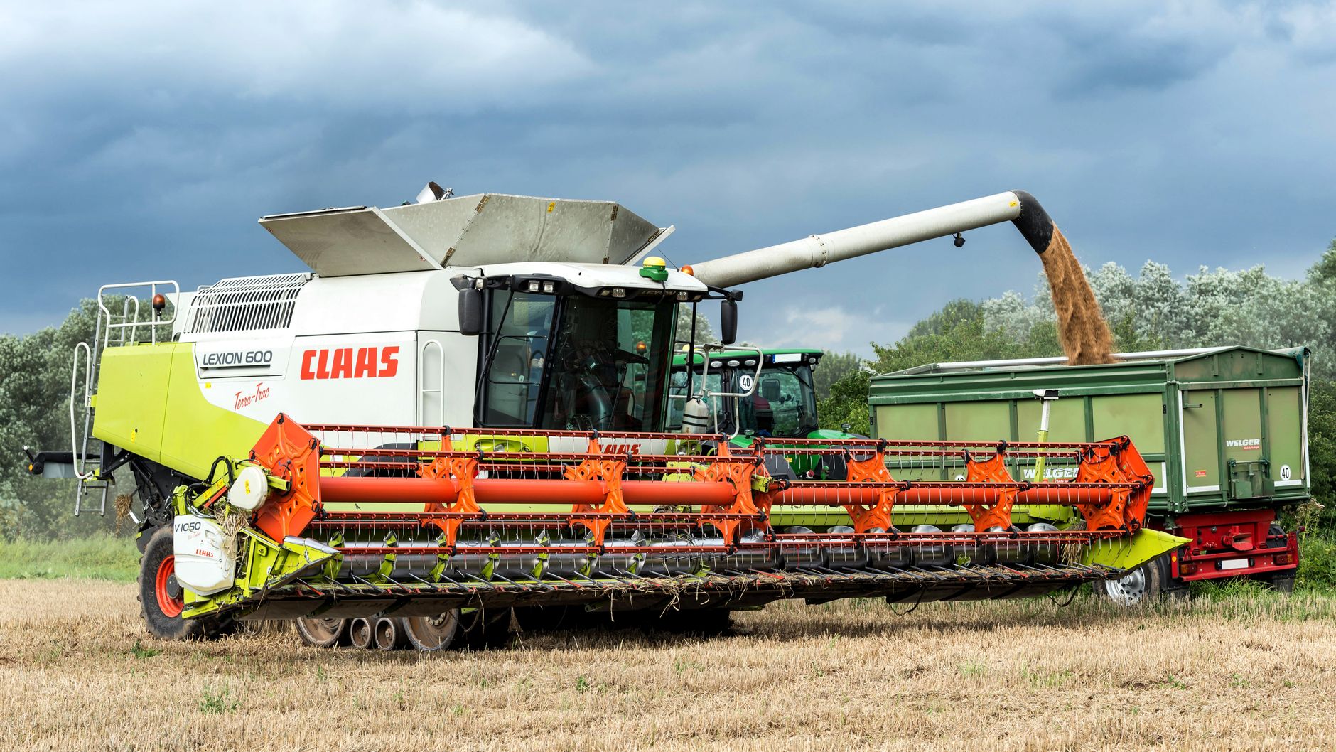 A combine harvester working in a field, unloading grain into a trailer.