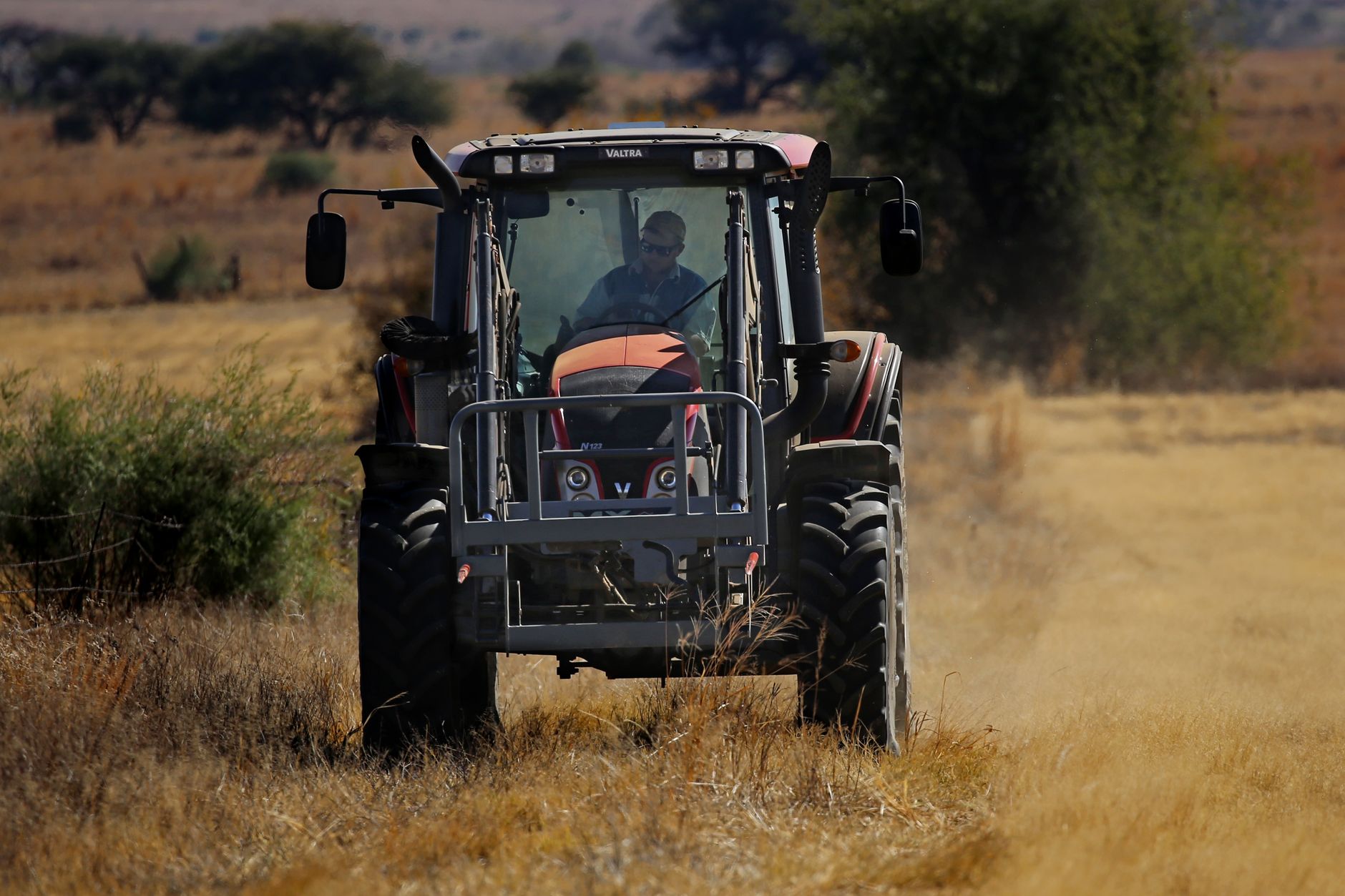 A farmer operates a tractor in a vast rural landscape, showcasing agricultural activity.