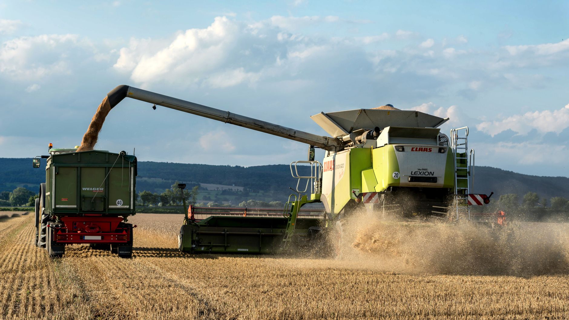 Combine harvester unloading grain into trailer in a rural field during harvest season.