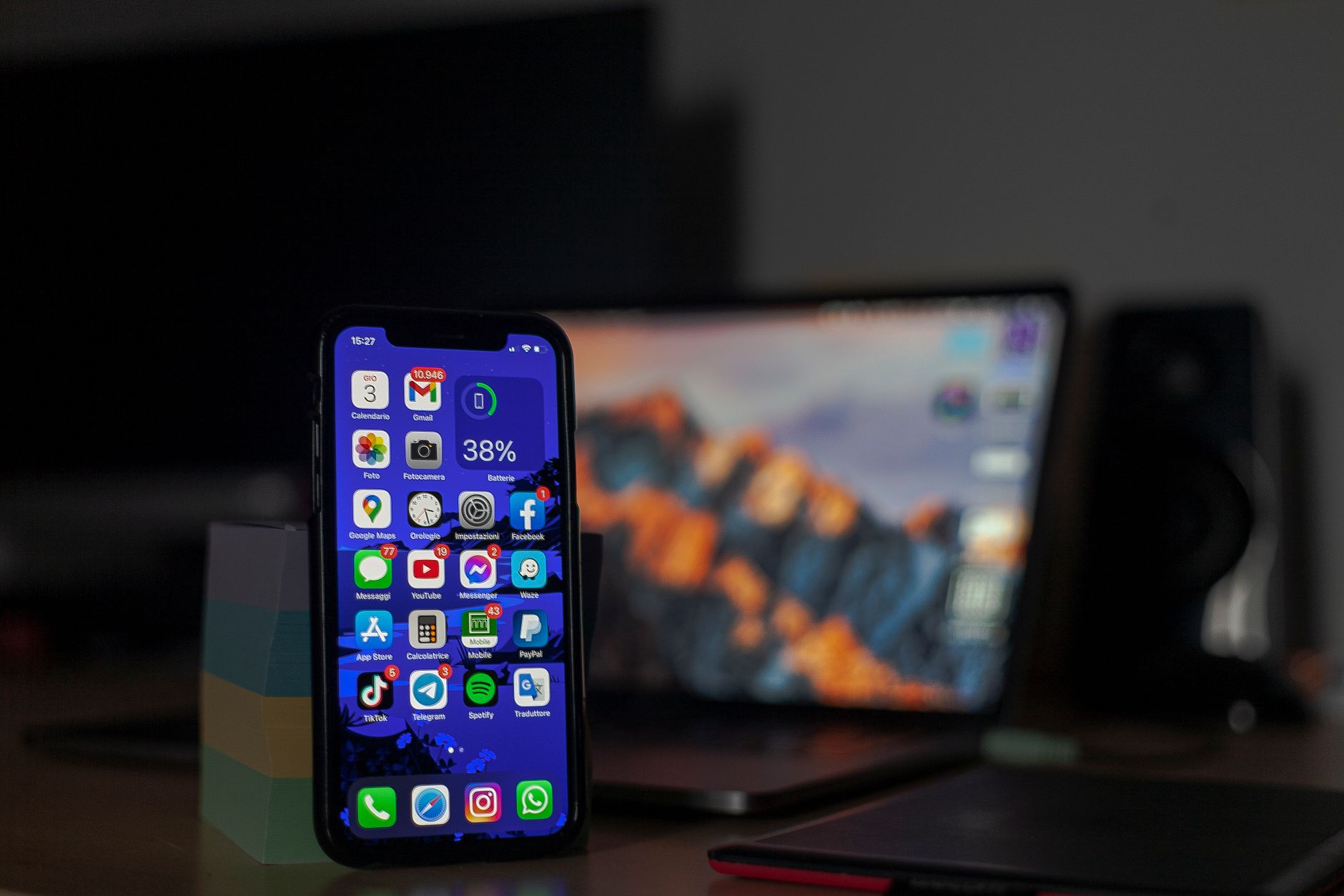 Smartphone displaying various apps in focus with a blurred laptop in the background.