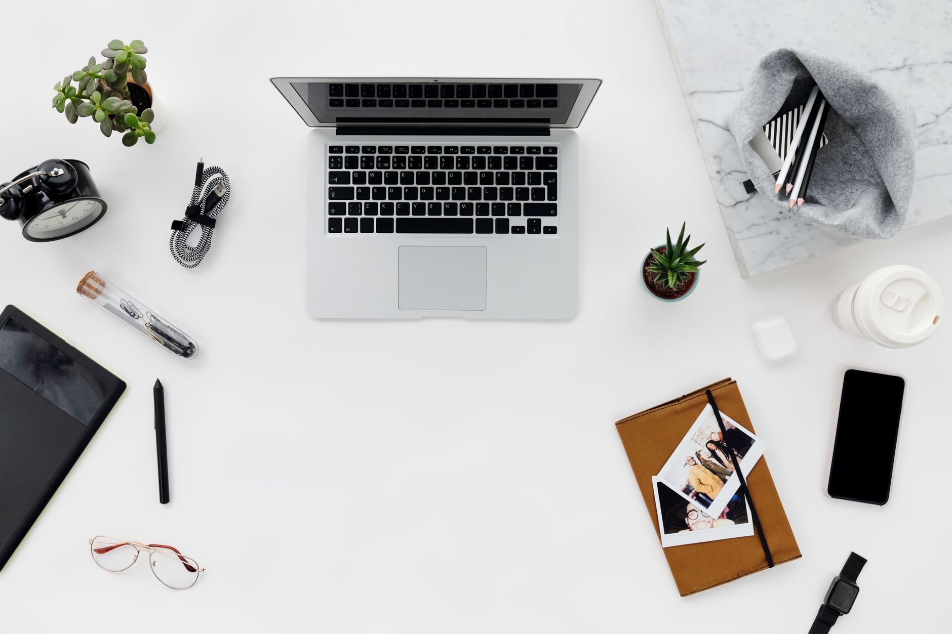 Top view of a minimalist workspace featuring a laptop, gadgets, and stationery on a clean desk.