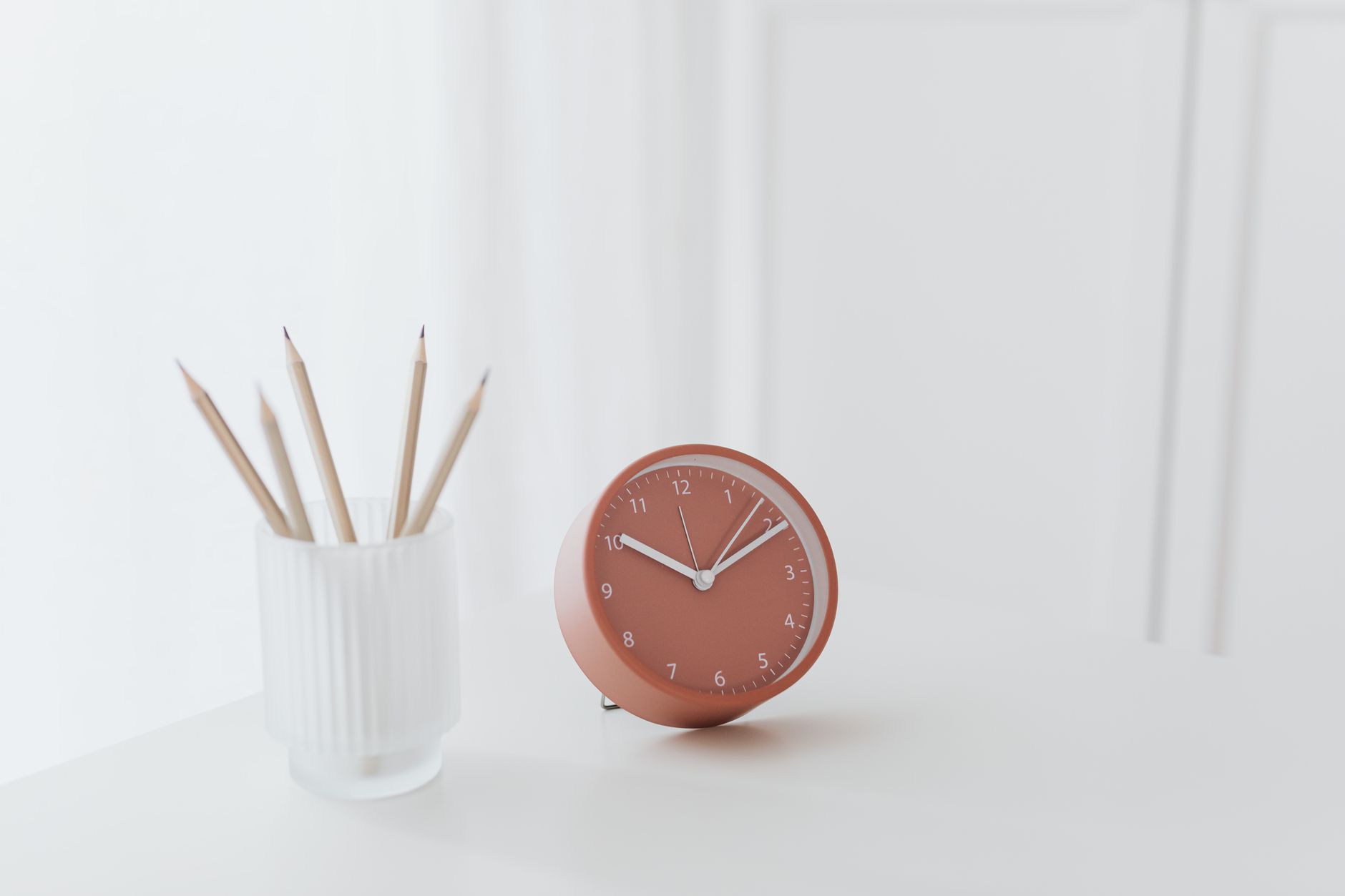 Minimalist desk with a red clock and pencils in a holder, perfect for a modern workspace.