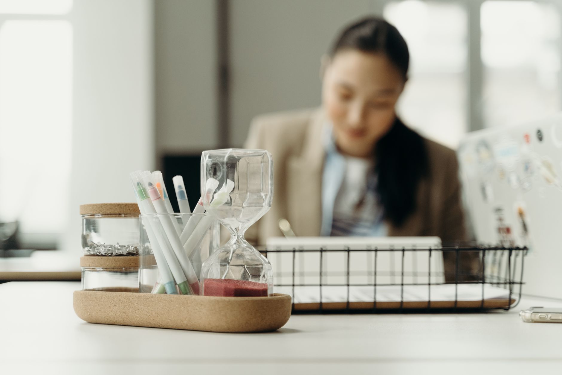 Close-up of a modern office desk with an hourglass and pens, emphasizing productivity and creativity.