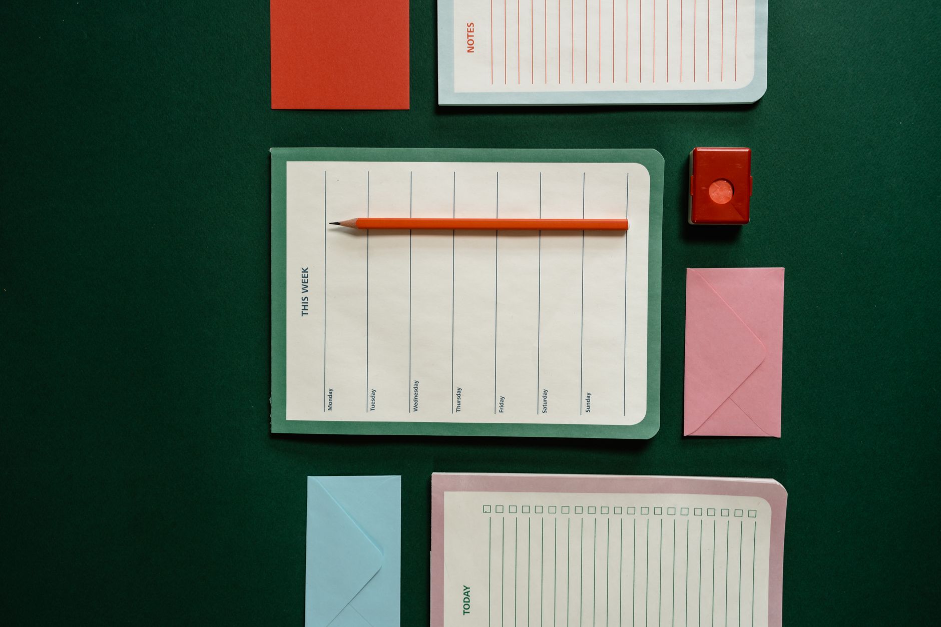 Flat lay of stationery items including planners, envelopes, pencil, and note cards on green surface.