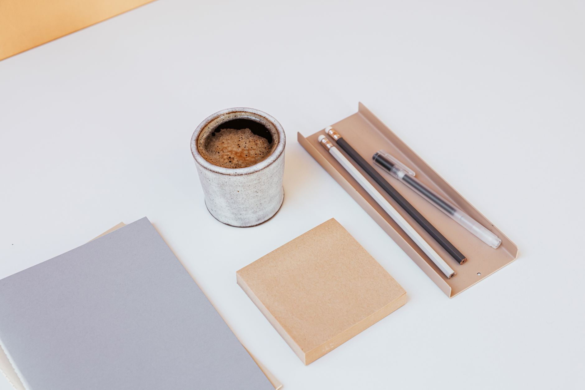 A minimalist desk setup featuring coffee, notebooks, and writing tools on a white surface.