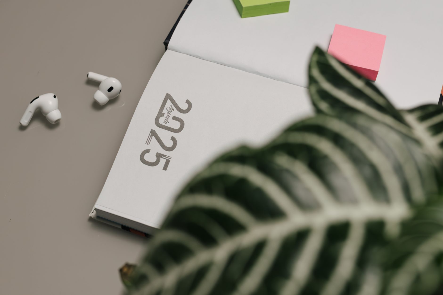 Open 2025 planner with AirPods and sticky notes, creating a modern workspace vibe.