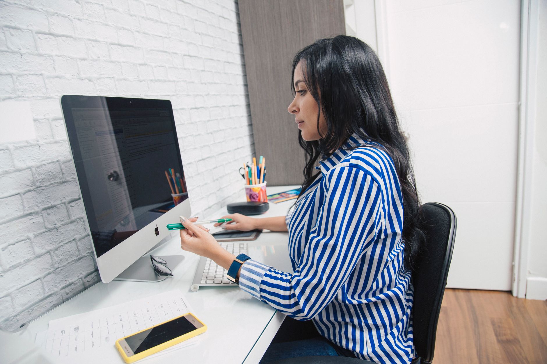 Woman in a striped shirt working at a computer desk in an office setting.