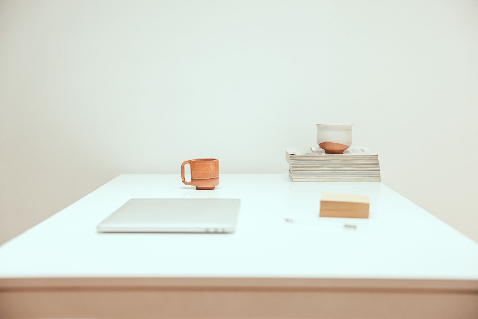 Simple minimalist workspace featuring a laptop, mug, and stacked magazines.
