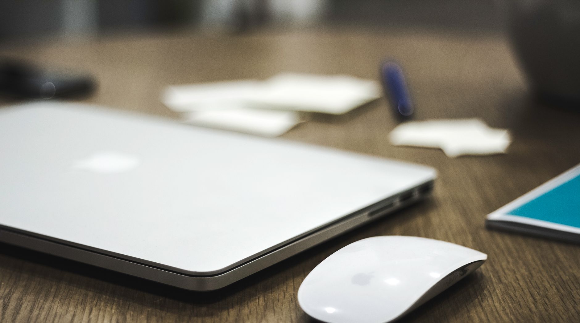 A clean and minimalist workspace featuring a closed laptop and wireless mouse on a wooden desk.