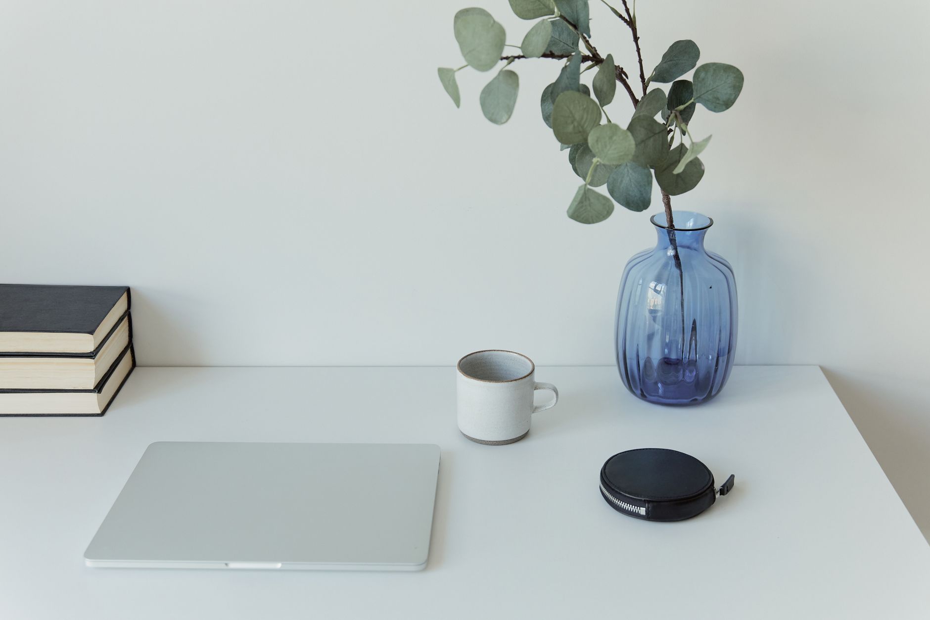 Clean minimalist desk featuring a laptop, blue vase with plant, and coffee mug.