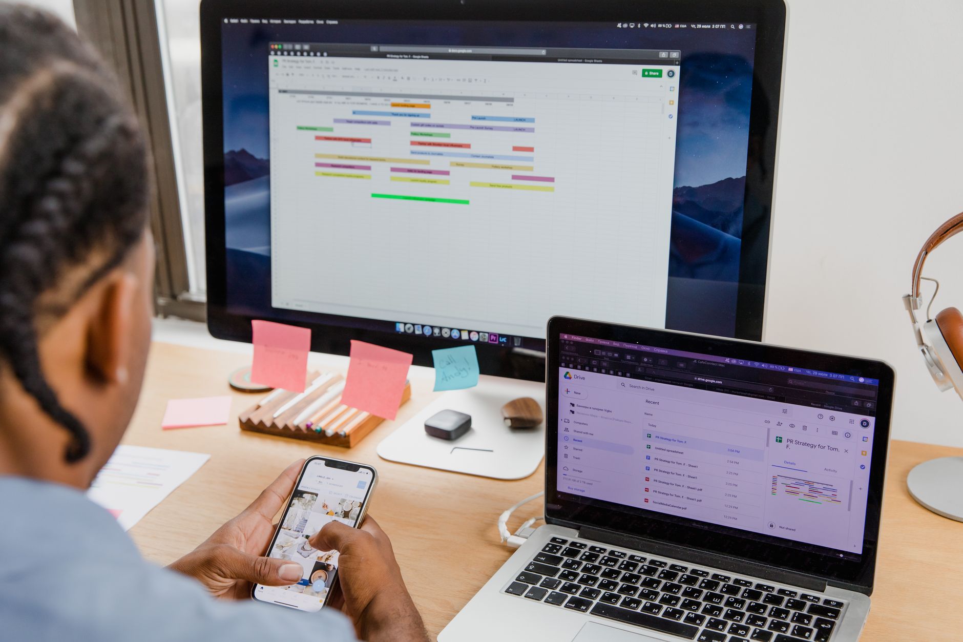 Businessman multitasks with smartphone, laptop, and monitor in office setting.