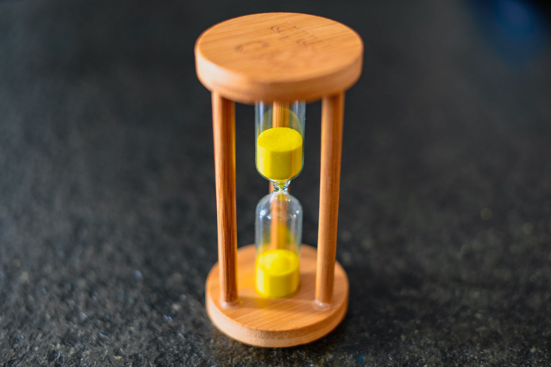 Close-up of a wooden hourglass with yellow sand on a dark textured surface.