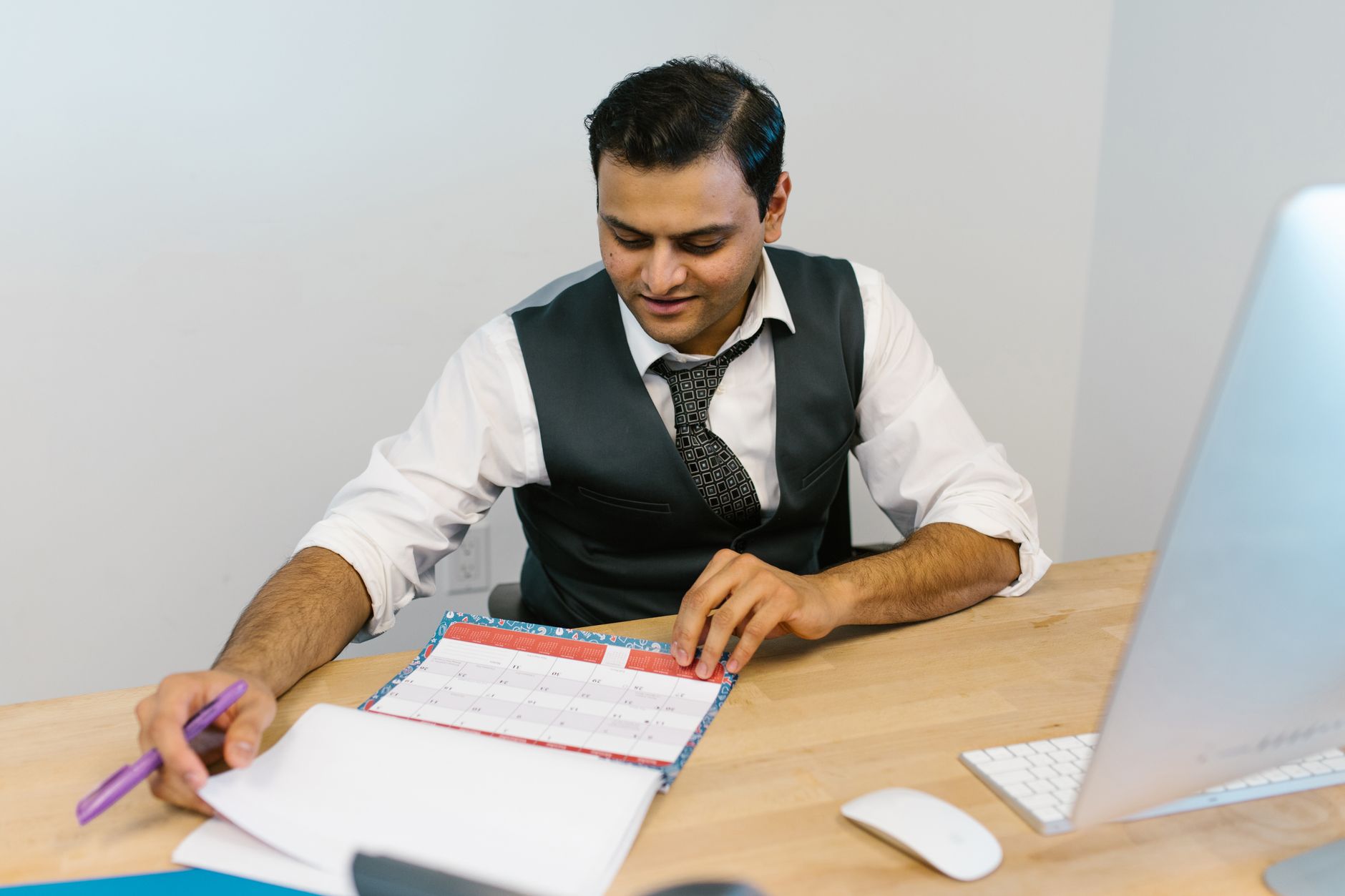 A businessman checks his schedule at a desk, referencing a calendar and making notes.