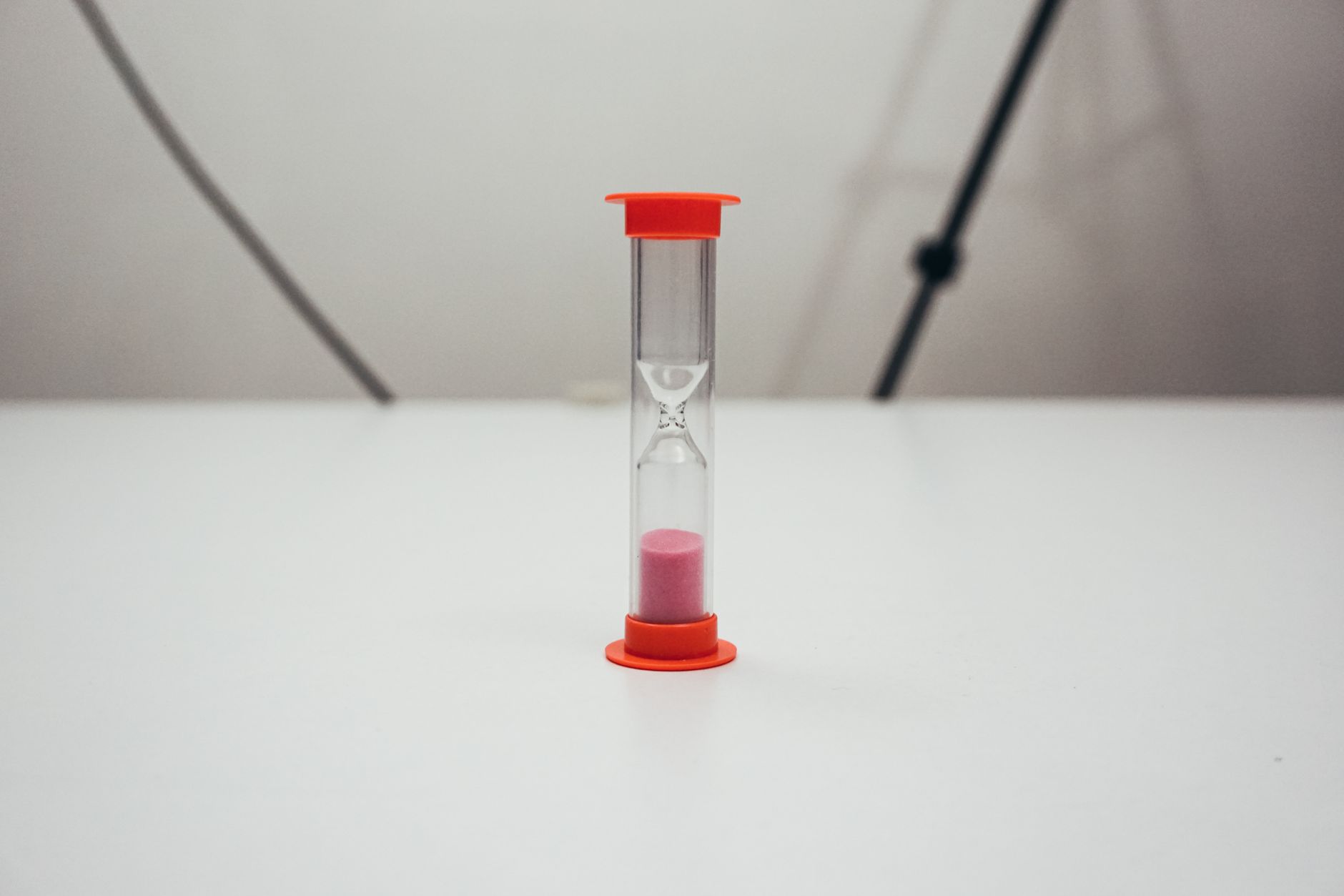 Close-up image of a red-topped hourglass filled with pink sand against a plain background.