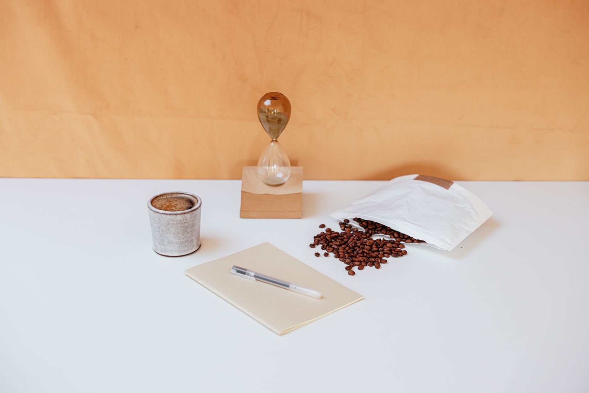 A minimalist workspace featuring coffee beans, an hourglass, a notebook, and a pen for creative inspiration.