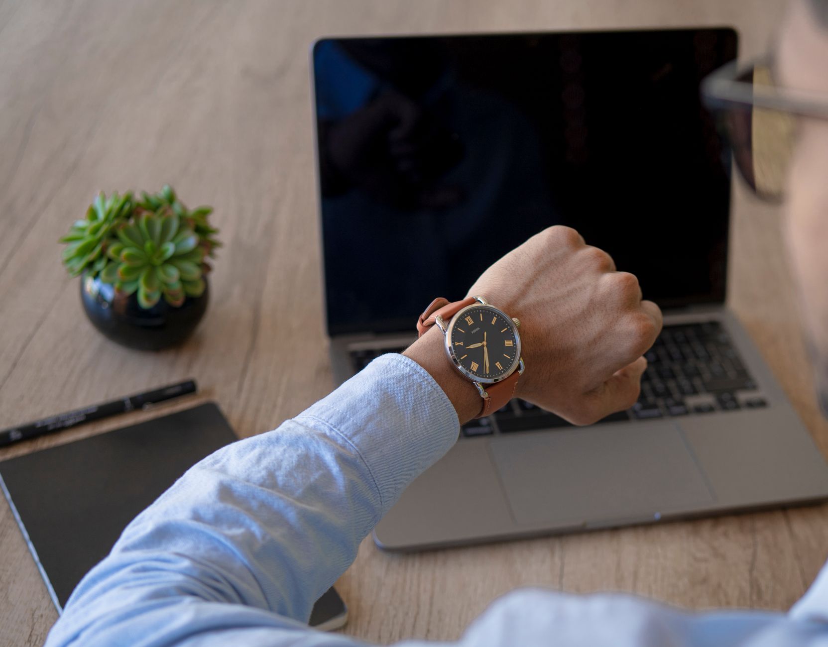 Adult male checks time on watch while working on a laptop at home office.
