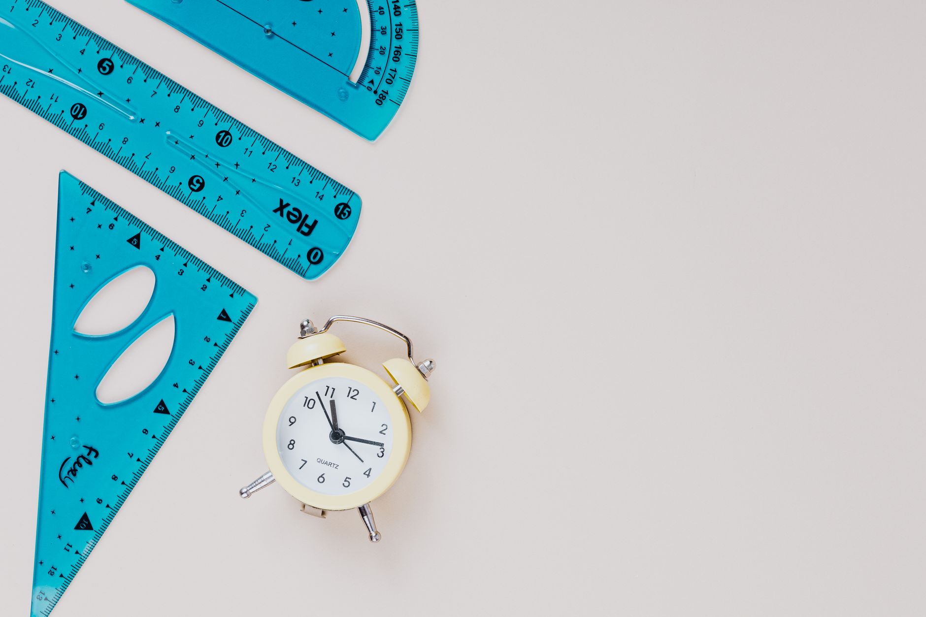 Yellow vintage alarm clock with rulers and triangles on a minimalist background.