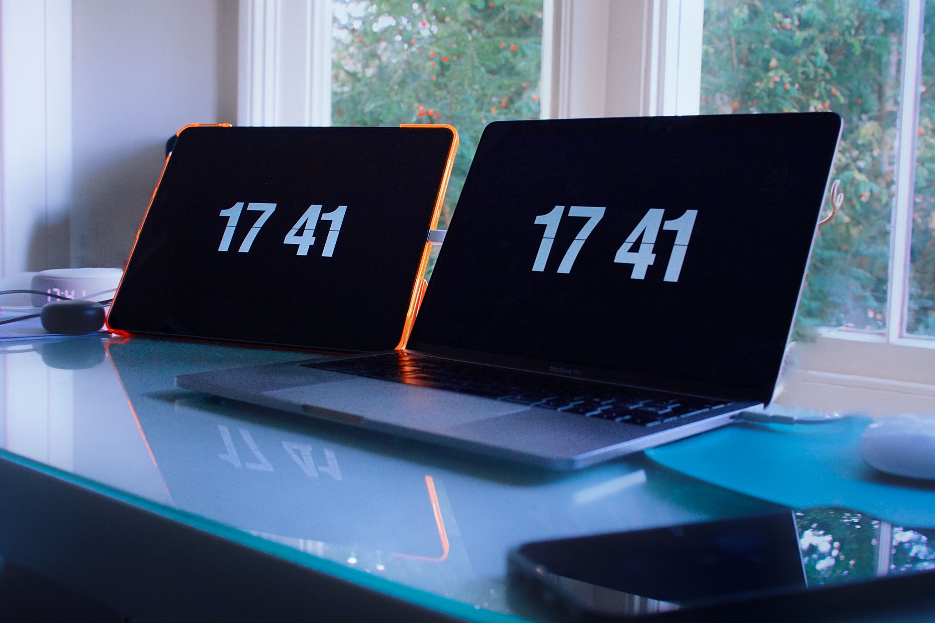 Laptops showing time 17:41 on glass desk, bright workspace.