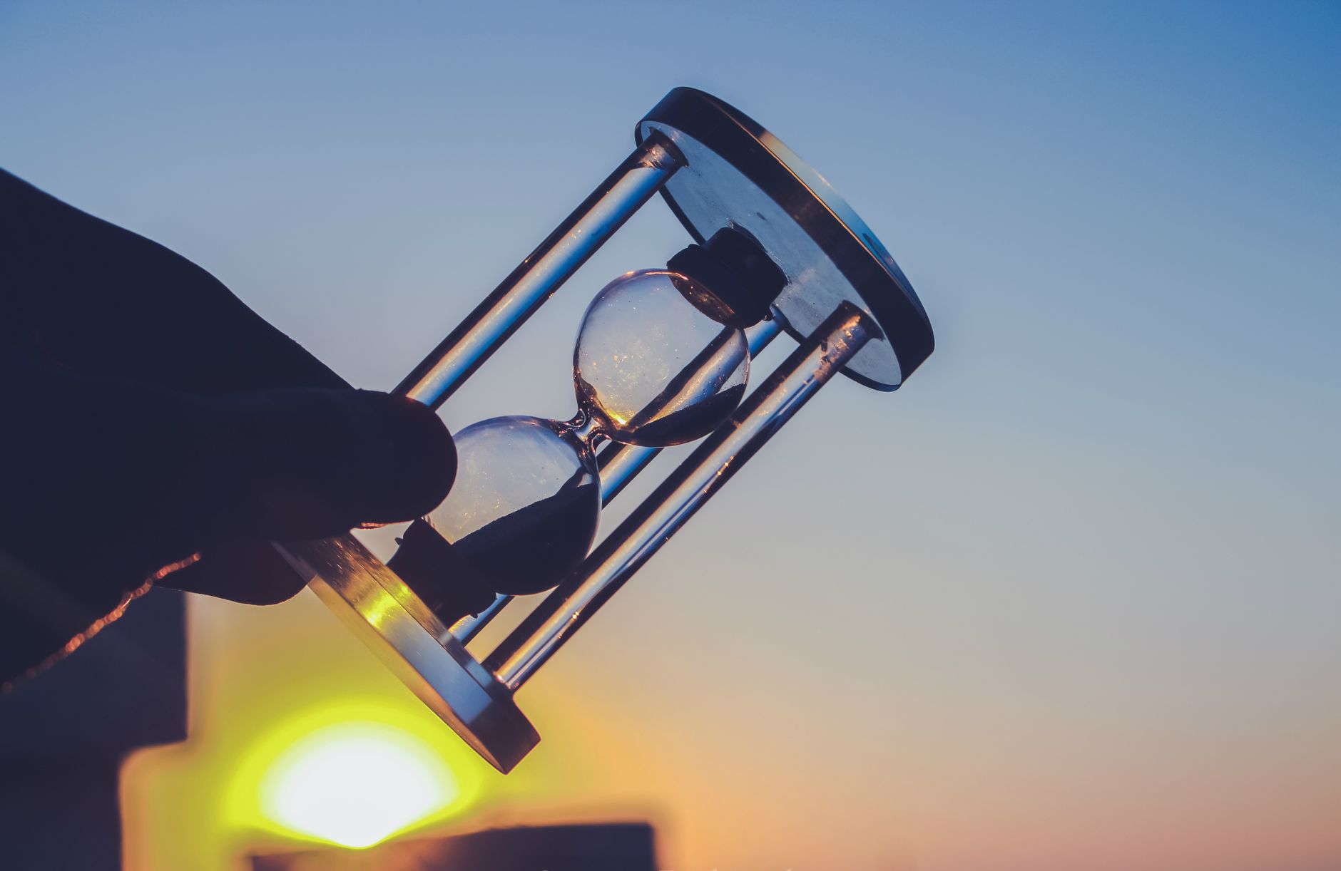 Silhouette of an hourglass held against a vibrant sunset sky in Syria. Time concept.