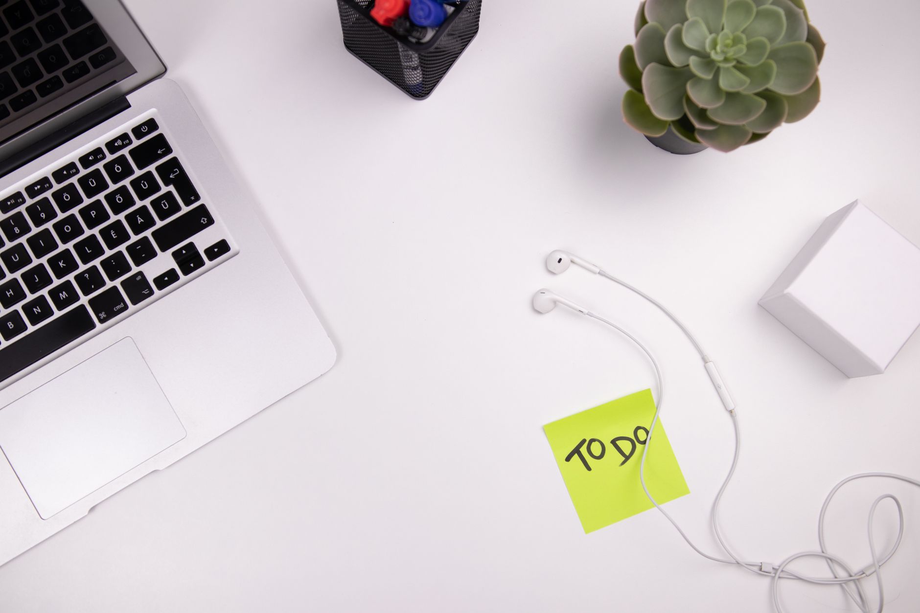 Organized workspace featuring a laptop, earphones, and a to-do list with plant decor.