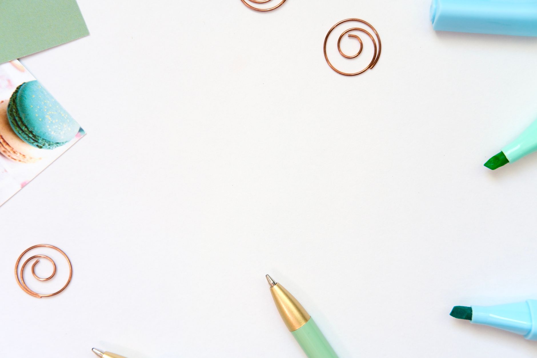 A minimalist flat lay image of stationery and a macaron, with ample white copyspace.