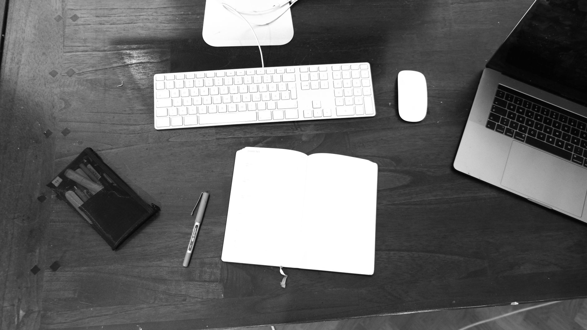Top view of opened modern netbook placed on wooden table near computer keyboard and mouse and opened notepad in workplace
