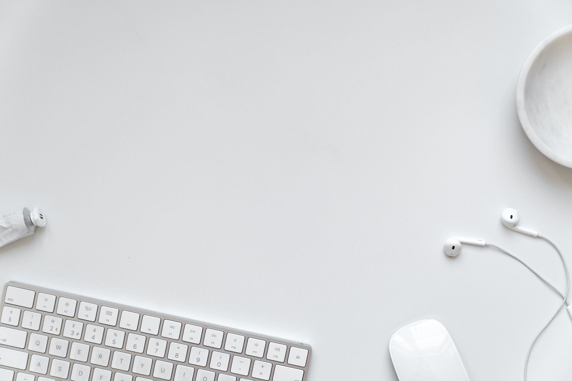 Clean and minimalist white desk setup with keyboard and earbuds.