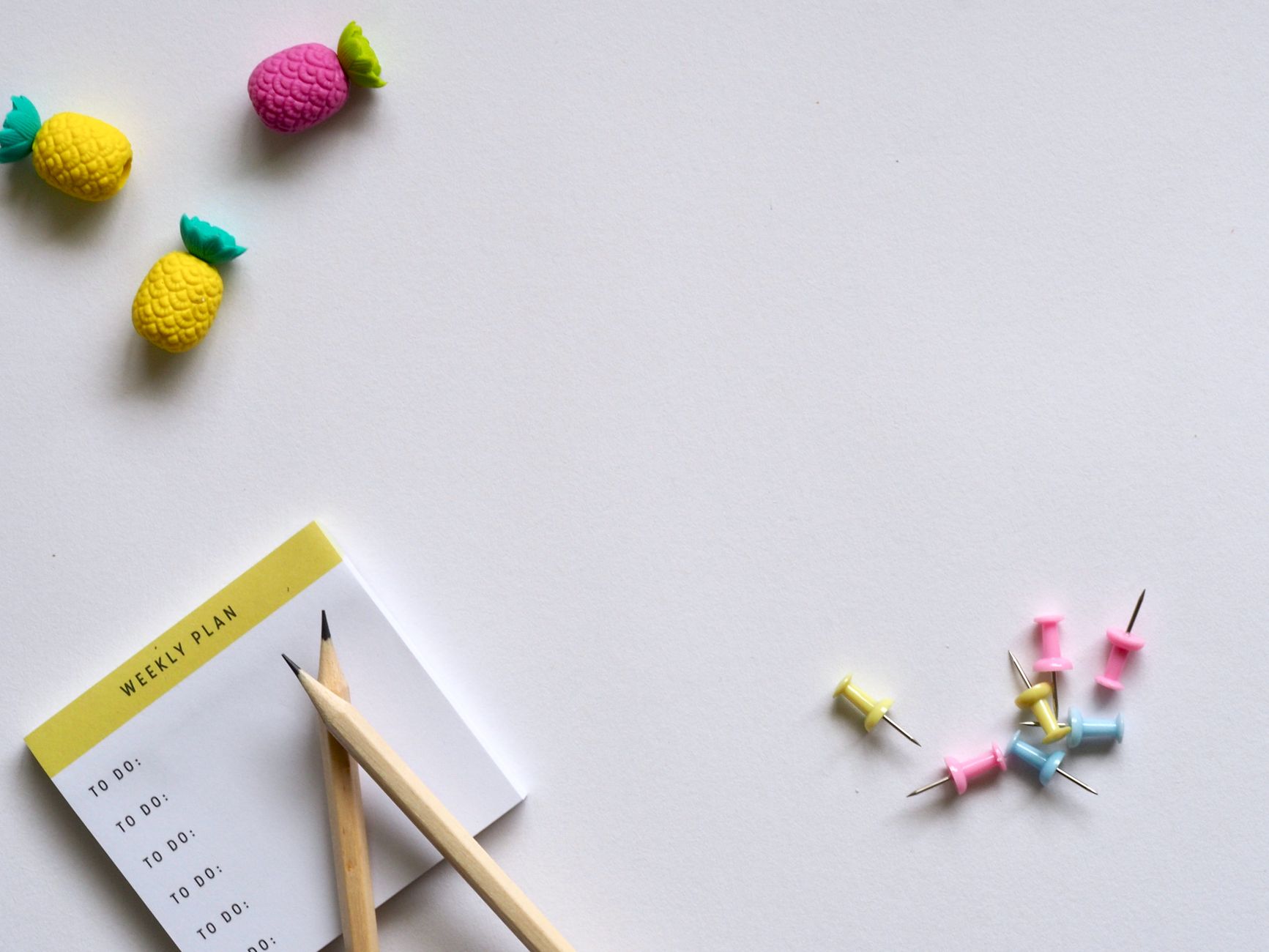 Flat lay of desk items including a planner, pencils, erasers, and push pins on a white background.