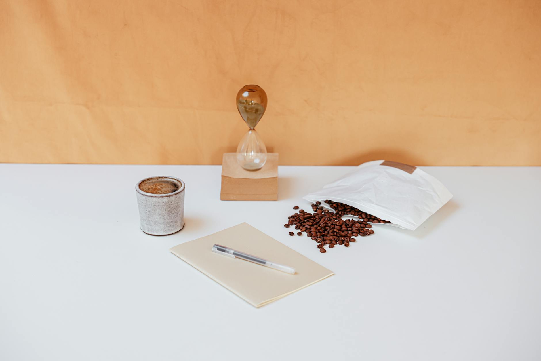 A minimalist workspace featuring coffee beans, an hourglass, a notebook, and a pen for creative inspiration.