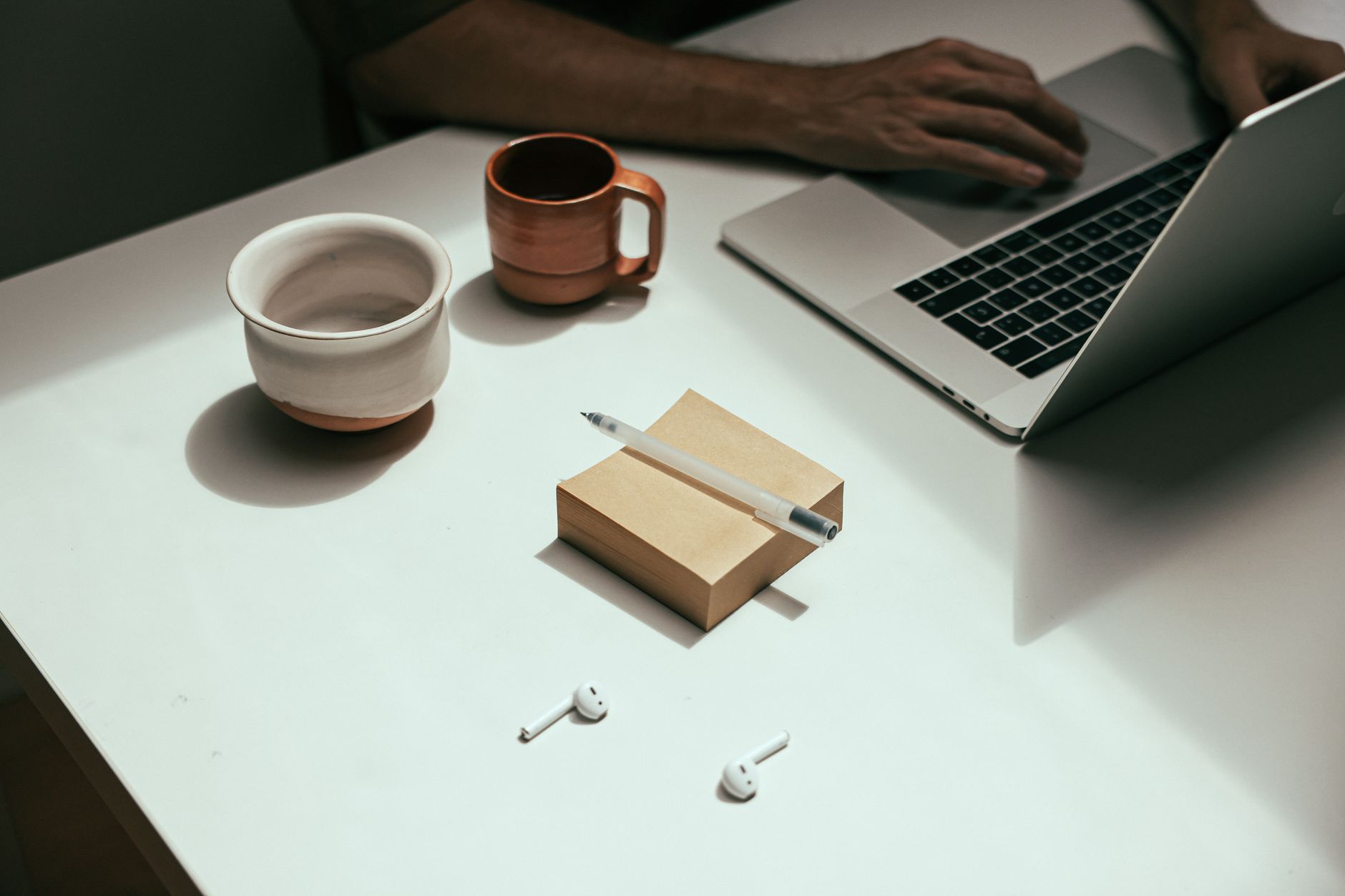 A stylish, minimalist workspace featuring a laptop, coffee cups, and wireless earbuds.
