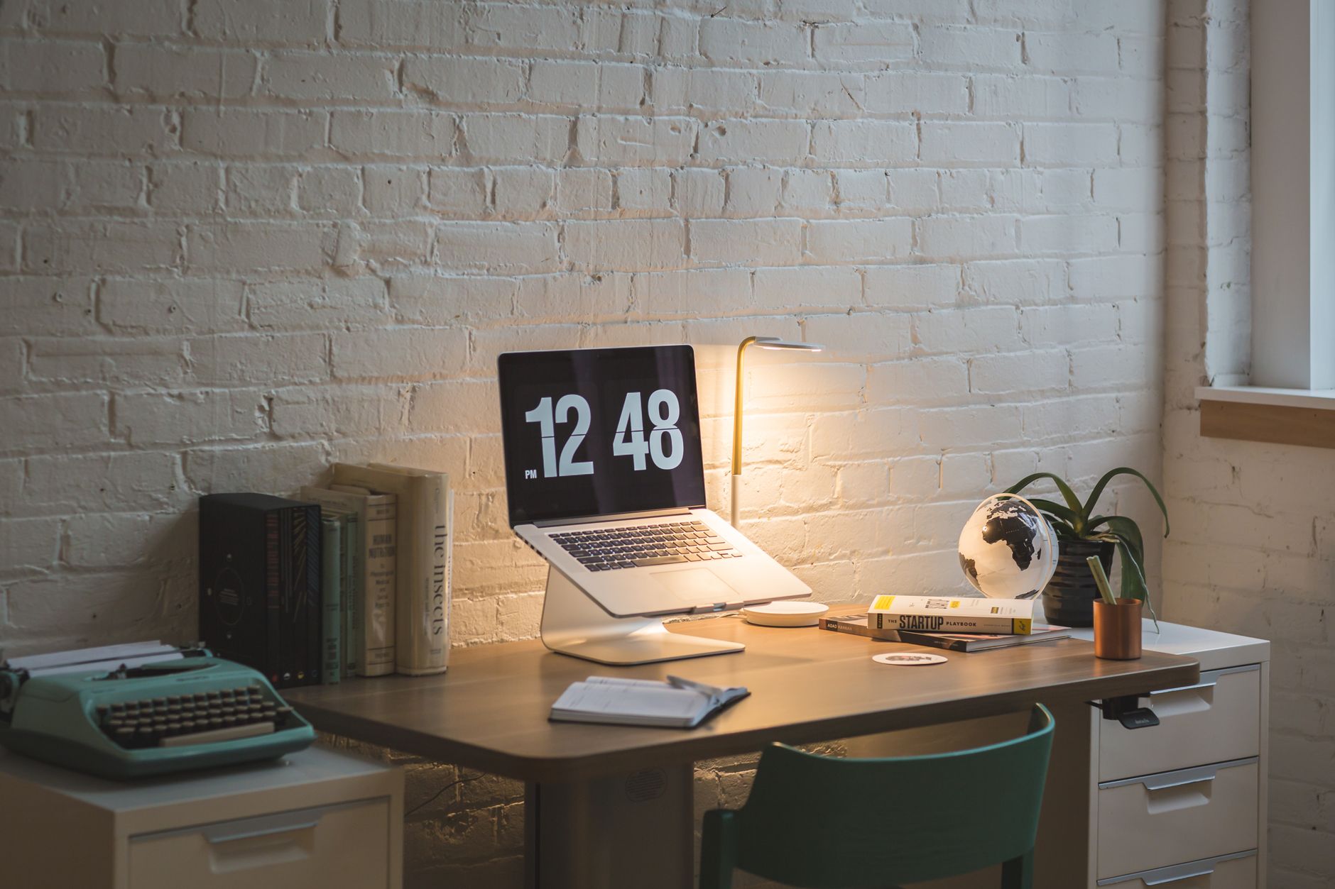 A well-organized workspace featuring a laptop, books, and a lamp on a wooden desk.